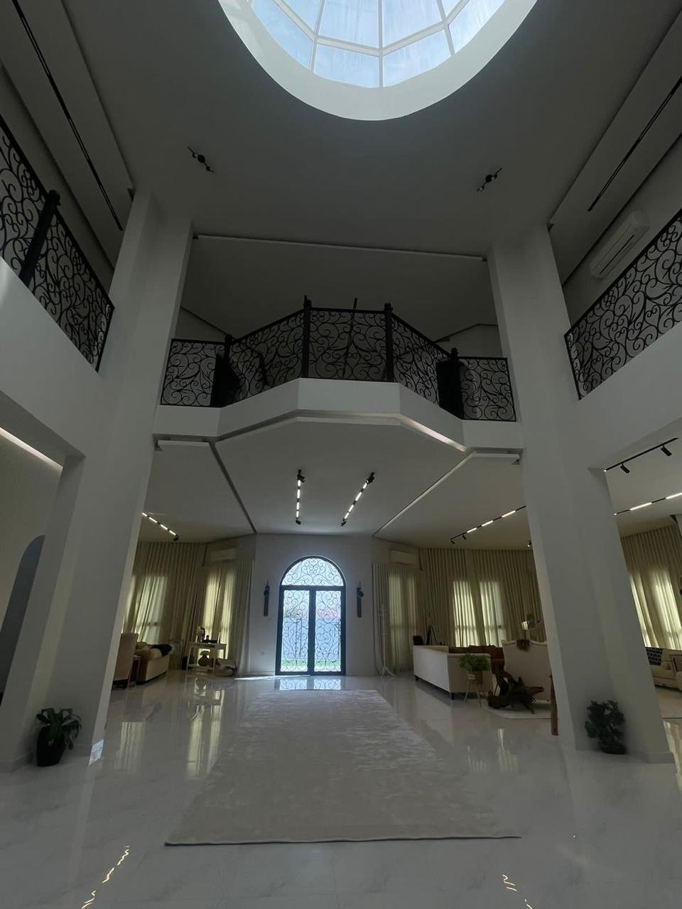 Double-height atrium with white columns, iron balustrades and a circular skylight overhead.