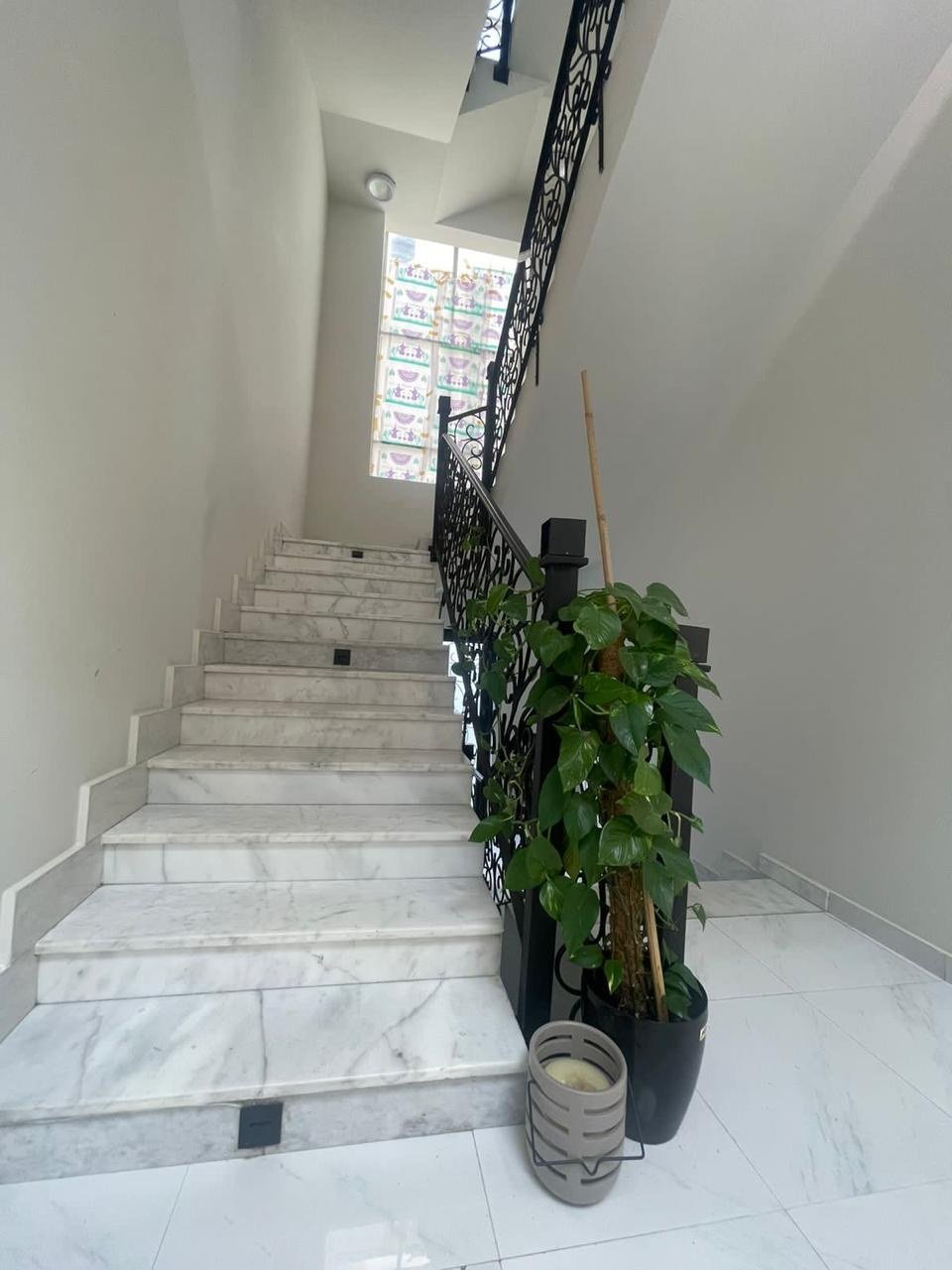 Marble staircase turning beneath a wrought-iron balustrade and tall window.