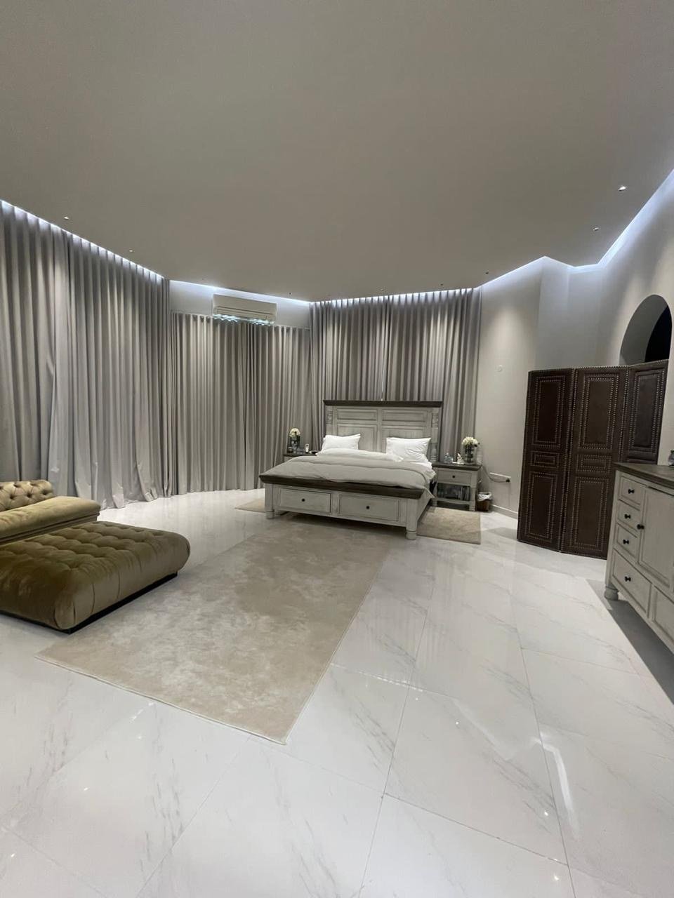 Master bedroom with floor-to-ceiling drapes lit by concealed cove lighting.