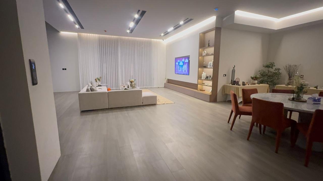 Open-plan lounge and dining area with pale plank floors and recessed ceiling lighting.